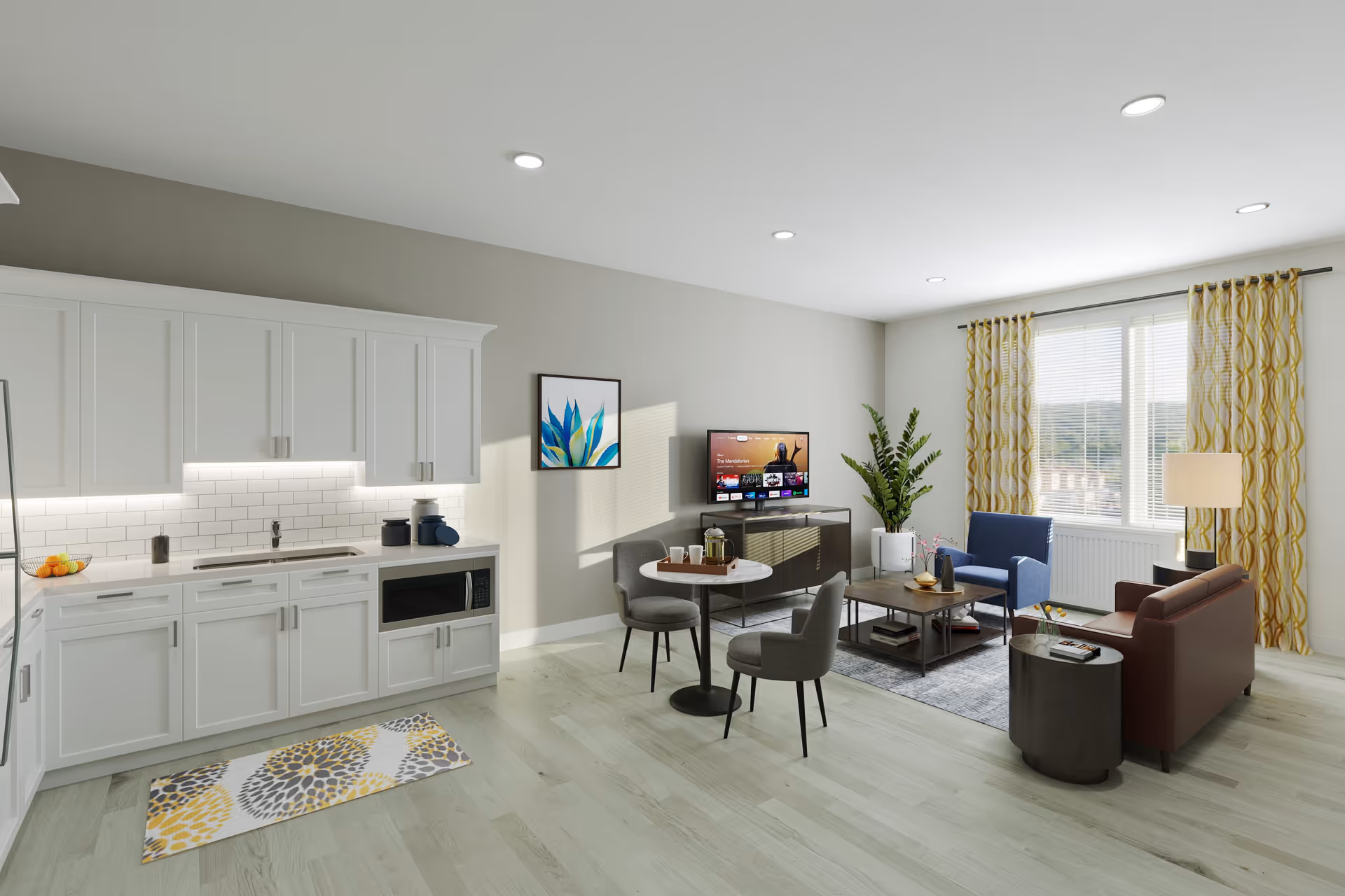A bright and modern living space featuring a kitchenette with white cabinets, a microwave, and a sink on the left side. Adjacent to the kitchenette is a small round dining table with two gray chairs. The living area includes a brown sofa, a blue armchair, a coffee table, a side table with a lamp, a flat-screen TV mounted on a stand, and a large window with yellow patterned curtains. A potted plant and framed artwork add decorative touches to the room.