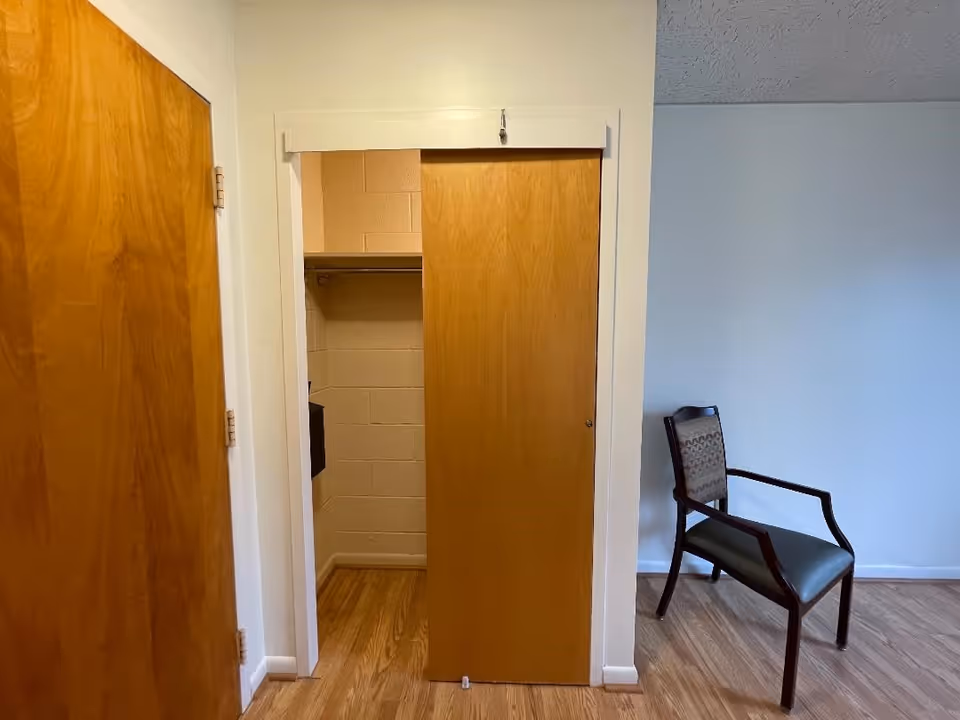 Interior room with a partially open wooden sliding closet door, adjacent wooden door, and a single upholstered chair on wood flooring.