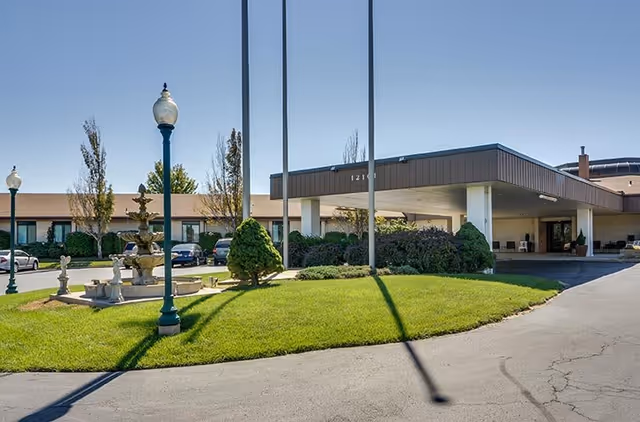 Front entrance of SummitView Terrace with a covered porte-cochere, circular driveway, manicured lawn, fountain, and lamp posts.