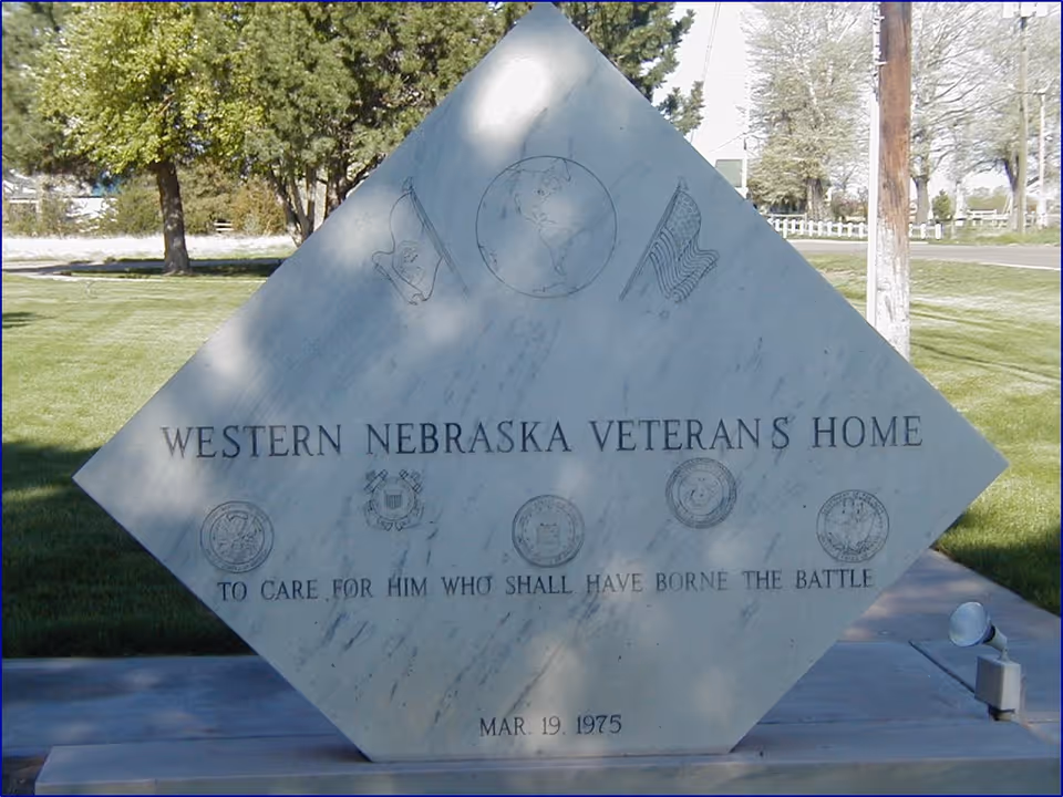 Diamond-shaped stone monument engraved with "Western Nebraska Veteran's Home" on a lawn with trees in the background.