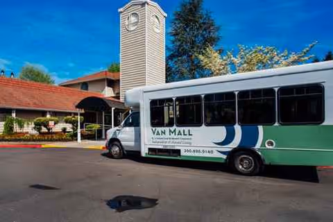 A green-and-white Van Mall retirement bus sits in front of a building with a clock tower.