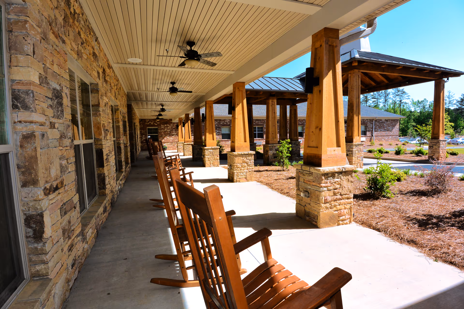Covered outdoor porch with wooden rocking chairs, stone building facade, and large wooden columns.