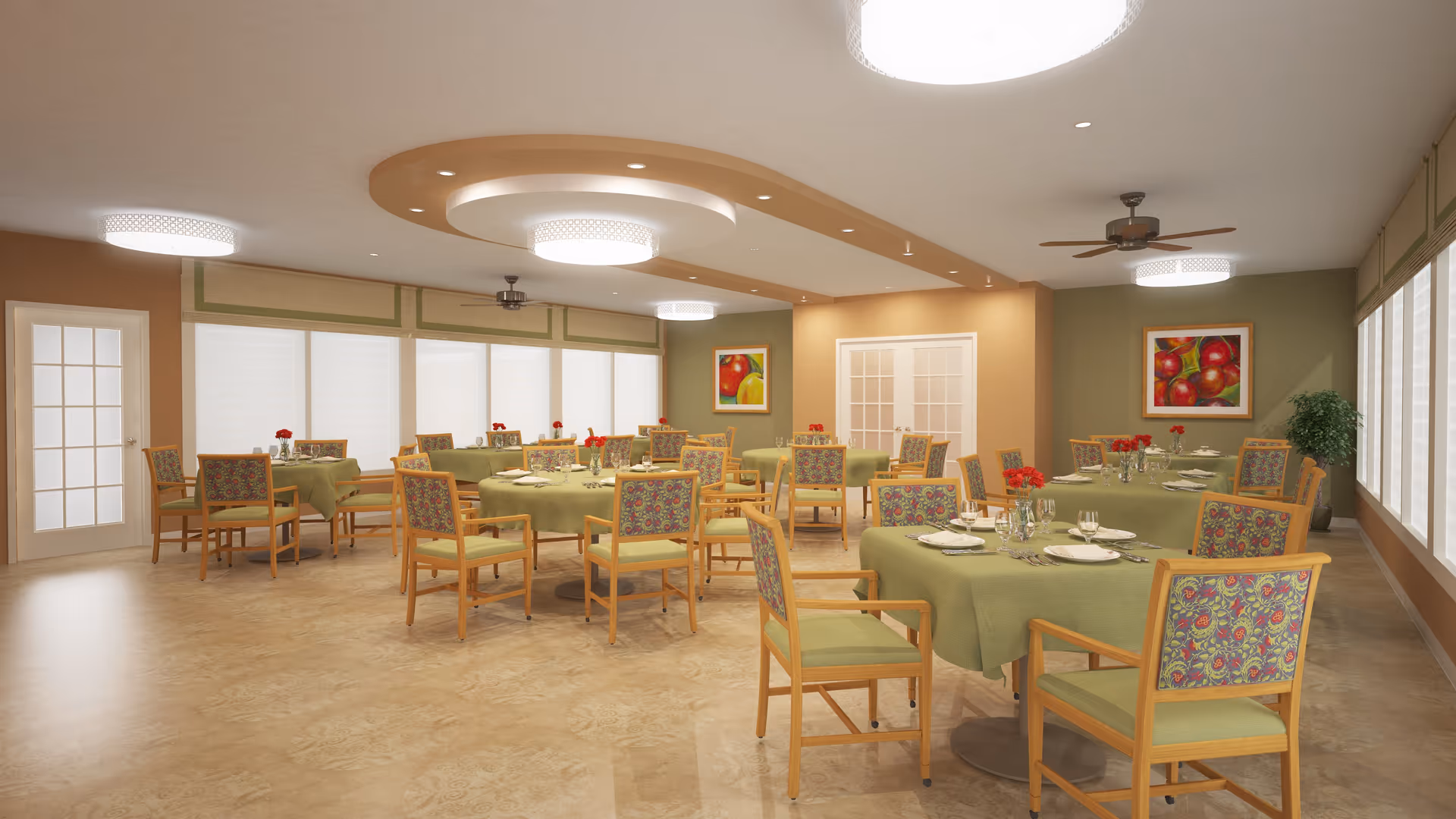 A spacious dining room with multiple round tables covered with green tablecloths, each set with plates, glasses, and napkins. Wooden chairs with floral patterned cushions surround the tables. The room has large windows with white blinds, beige walls, ceiling fans, and modern circular ceiling lights. There are framed paintings of apples on the walls and a potted plant in the corner.