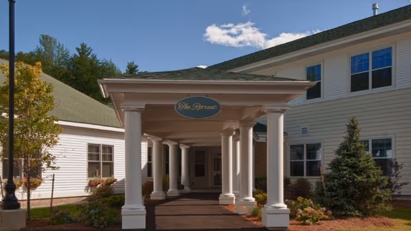 Covered portico with white columns at the entrance of a light-colored two-story senior care building.