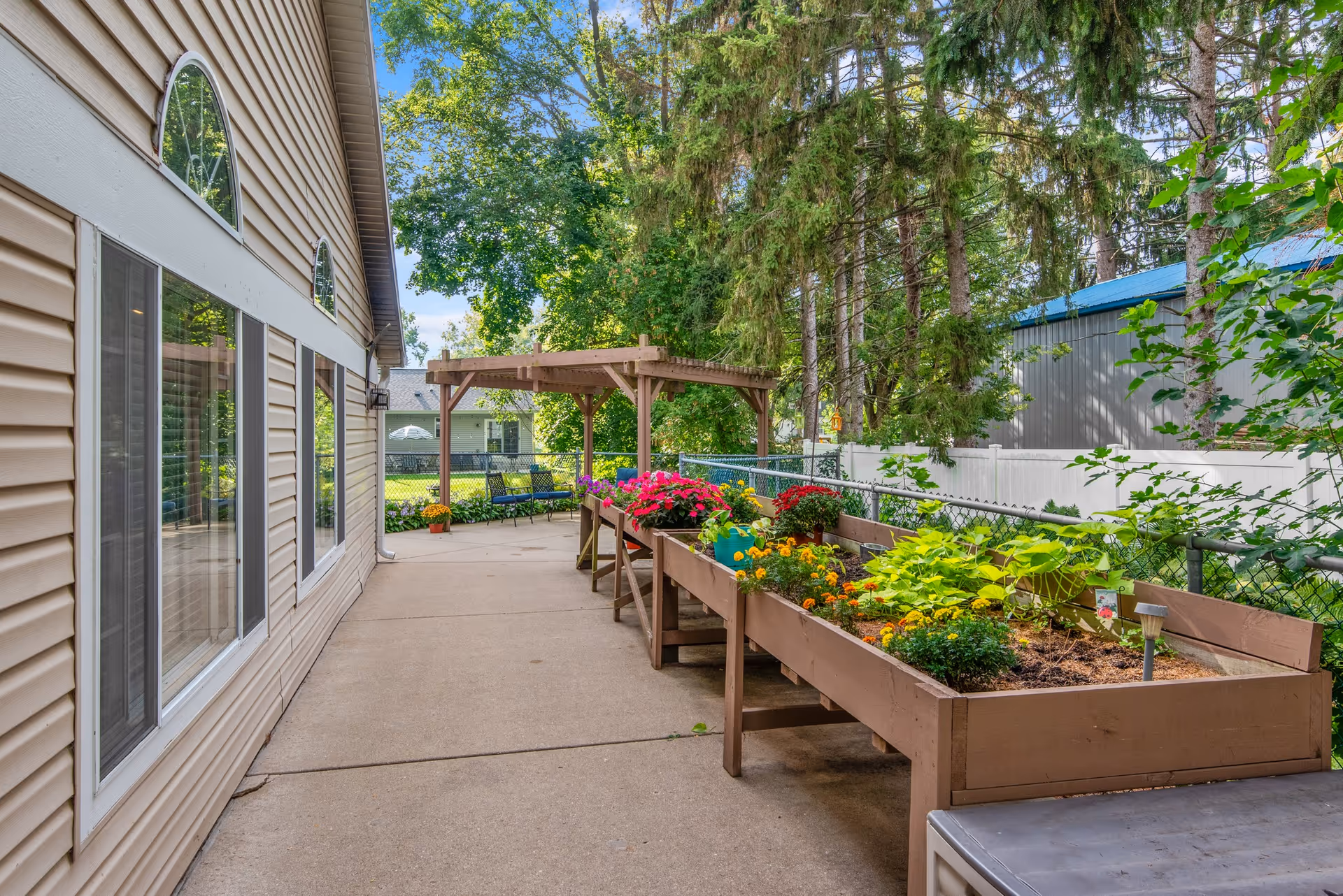 Outdoor patio beside a building with raised planter boxes filled with flowers and a wooden pergola.