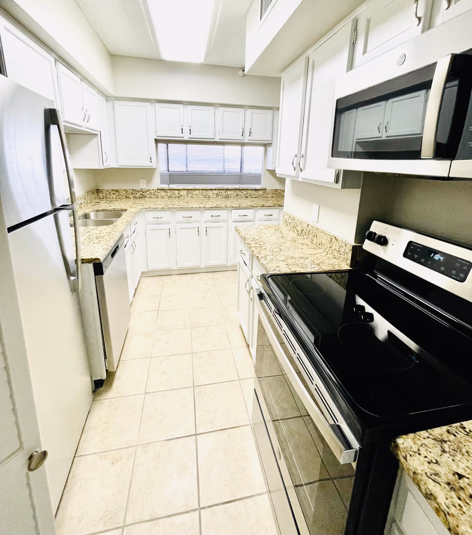 Bright galley kitchen with stainless steel appliances, white cabinets, and granite countertops.