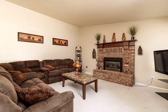 Cozy living room with brown sectional, brick fireplace, coffee table, TV, and wall art.