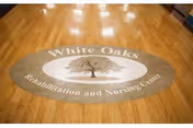 A polished wooden floor with a large oval logo in the center that reads 'White Oaks Rehabilitation and Nursing Center' surrounding an image of a tree.