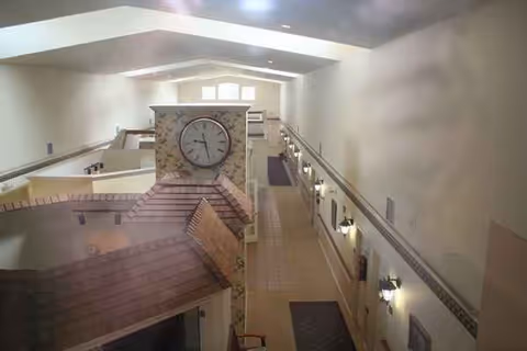 Interior atrium with a central clock on a brick column, staircases, and railings.