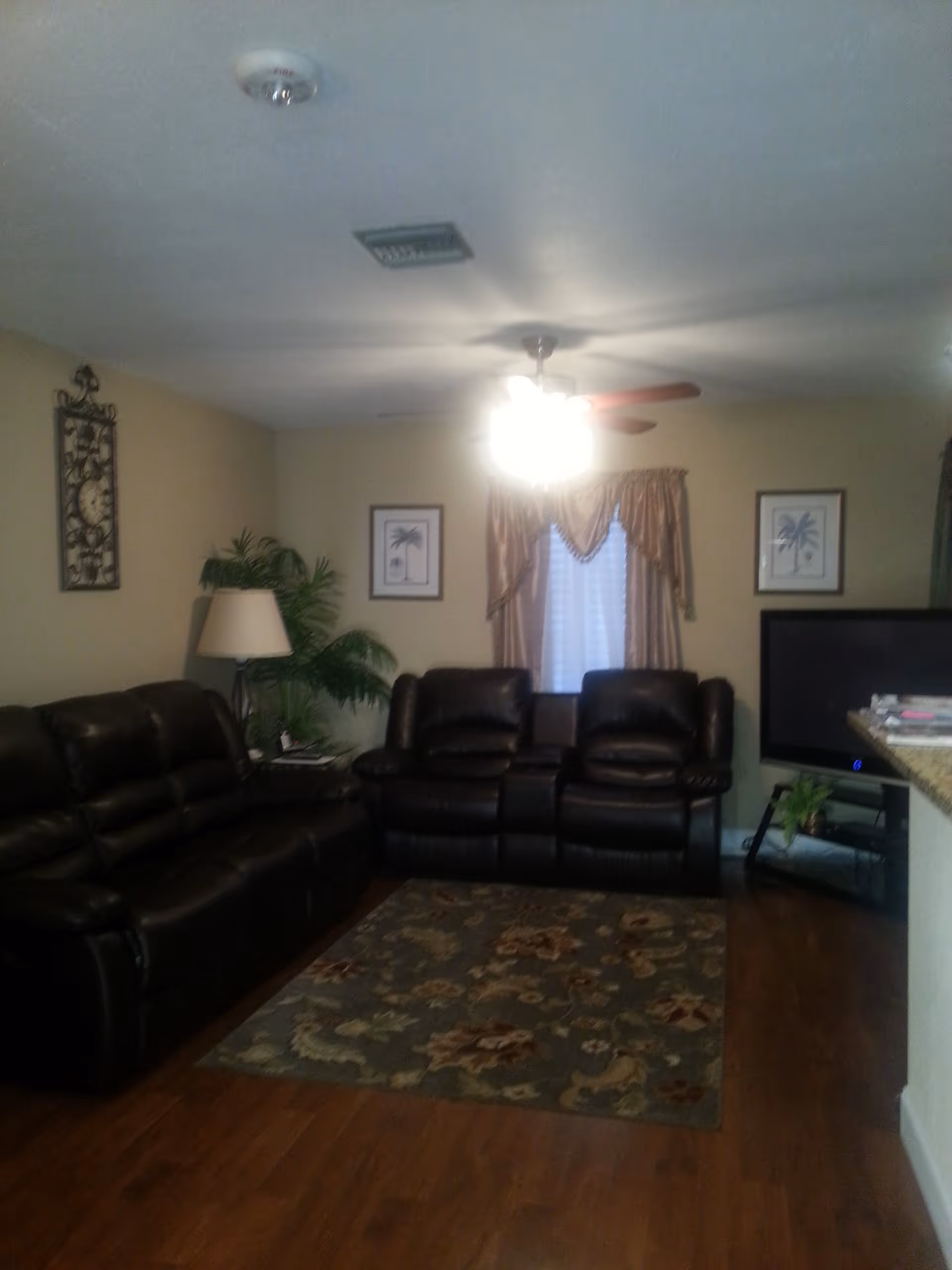 Cozy living room with dark leather recliners, a patterned area rug, TV, and a ceiling fan over hardwood floors.