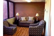 Small seating area with a sofa, two patterned armchairs, side tables with lamps, a brick accent wall and windows.