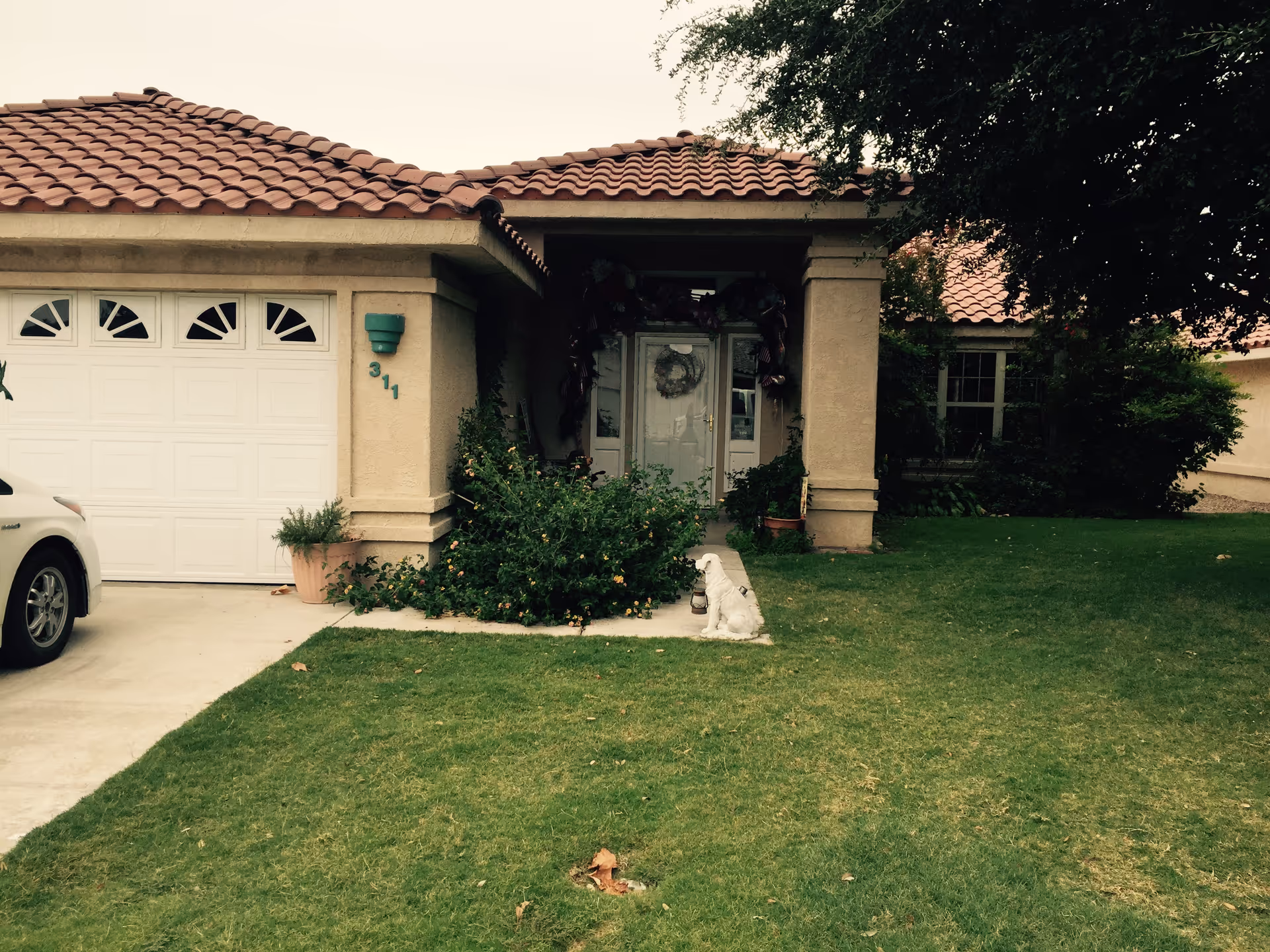 Front exterior of a single-story stucco house with a red tile roof, attached garage, and grassy front lawn.