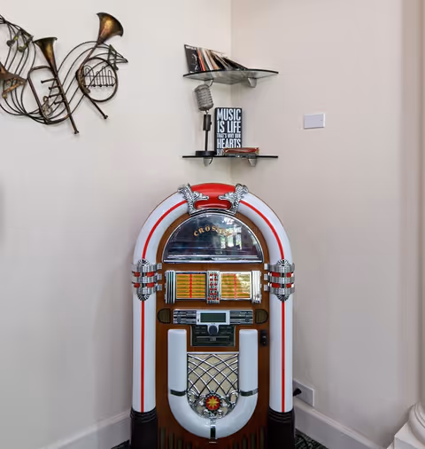A retro jukebox sits in a corner beneath glass shelves and musical wall art.