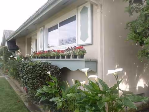 Exterior of a senior living facility with window boxes and lush greenery.