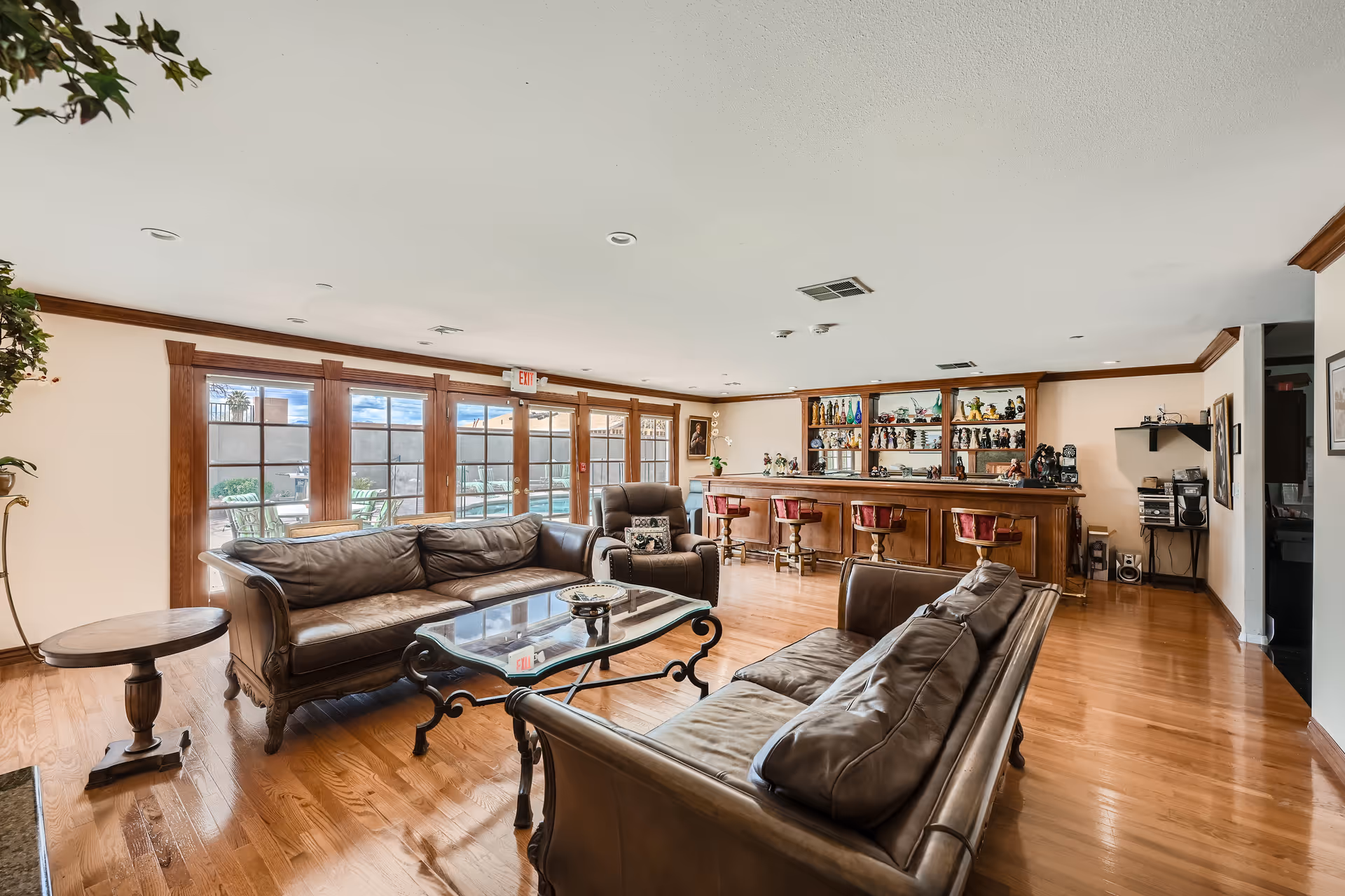 Bright communal lounge featuring leather sofas around a glass coffee table and a wooden bar with stools beneath large windows.