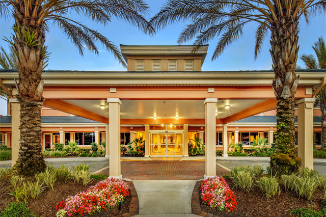 Covered main entrance of Fleet Landing with palm trees, flower beds, and an illuminated entryway.