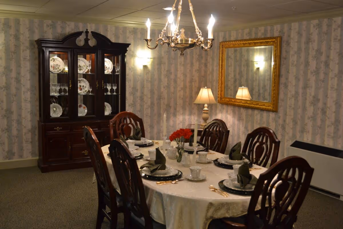 Formal dining room with a set table, wooden chairs, a china cabinet, chandelier and a mirror on patterned wallpaper.