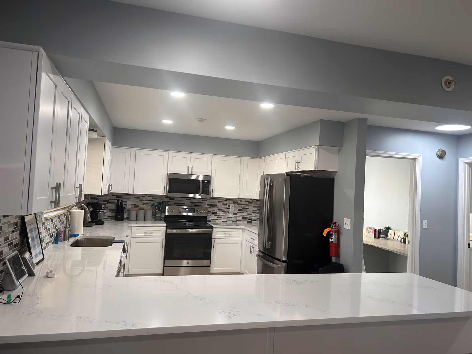 Bright modern kitchen with white cabinets, a marble-look island countertop, stainless steel refrigerator, oven and microwave, and a mosaic tile backsplash.