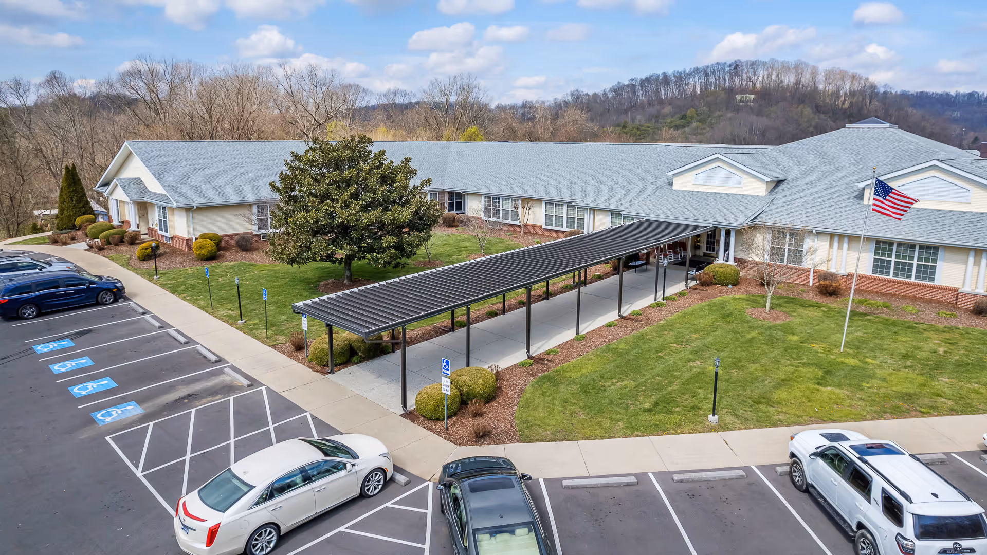 Exterior view of a senior living facility with a long covered walkway and a parking lot.