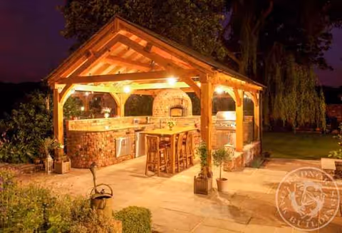 Outdoor brick kitchen pavilion at night with bar stools and grill.