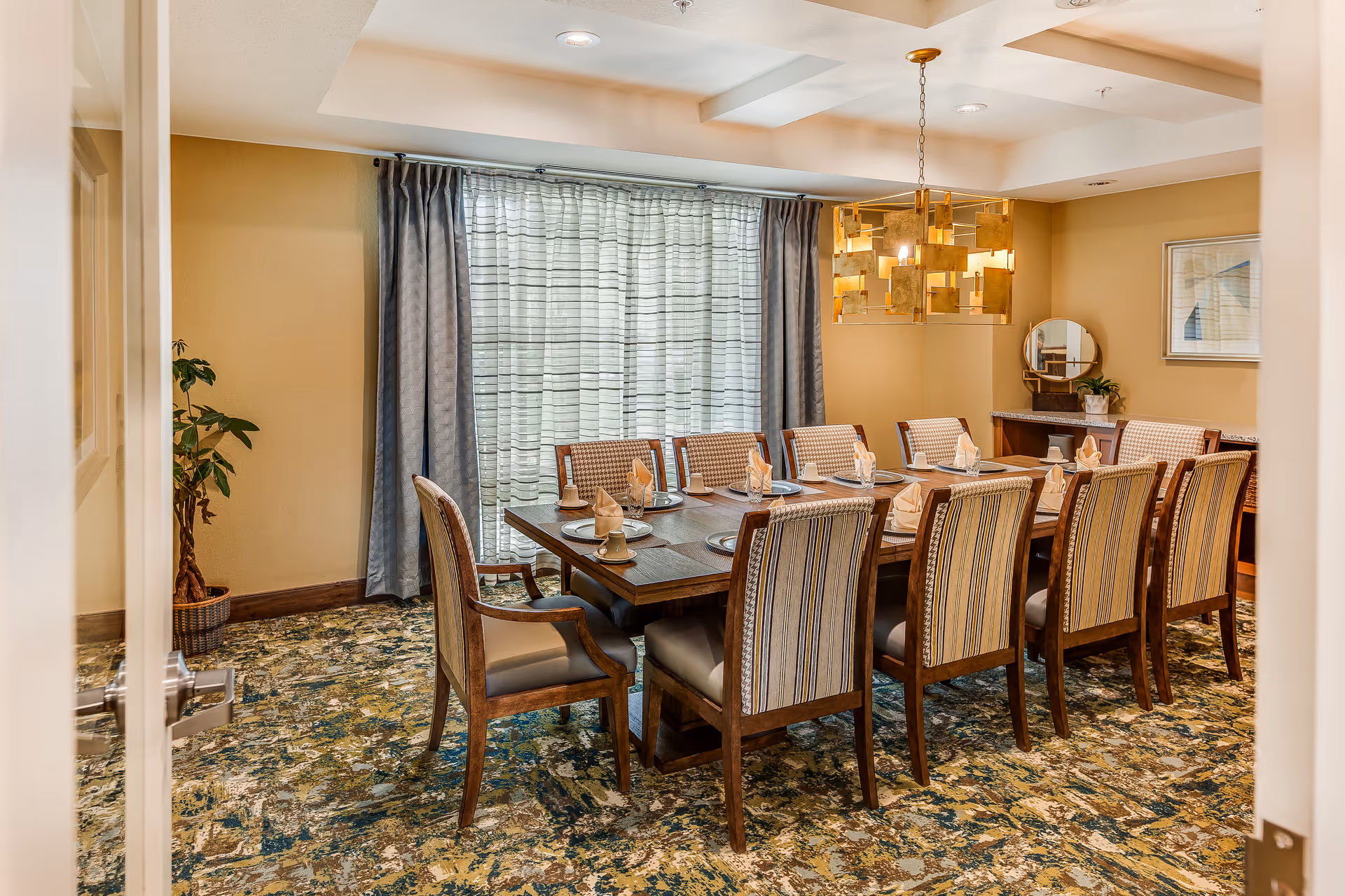 A formal private dining room with a long wooden table set for a meal, surrounded by upholstered chairs beneath a modern chandelier.