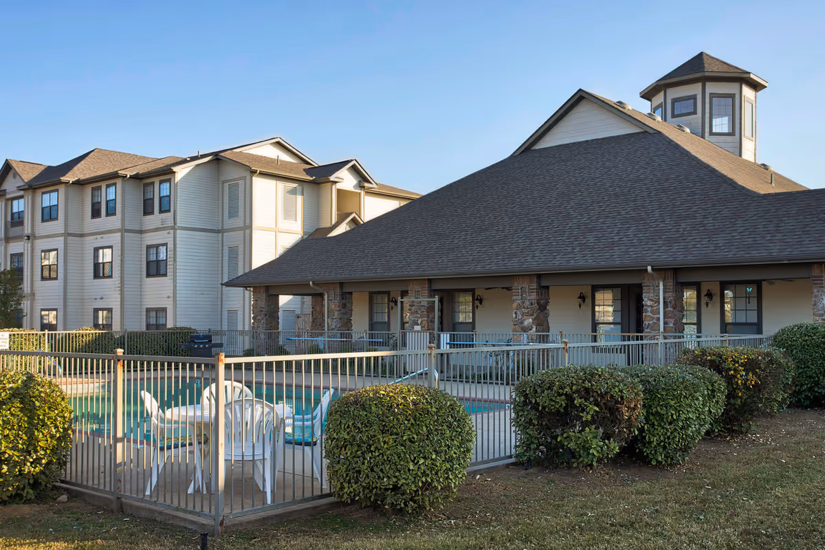 Exterior view of the HomeTowne at Conway building with a fenced outdoor pool, patio chairs, and landscaped shrubs.