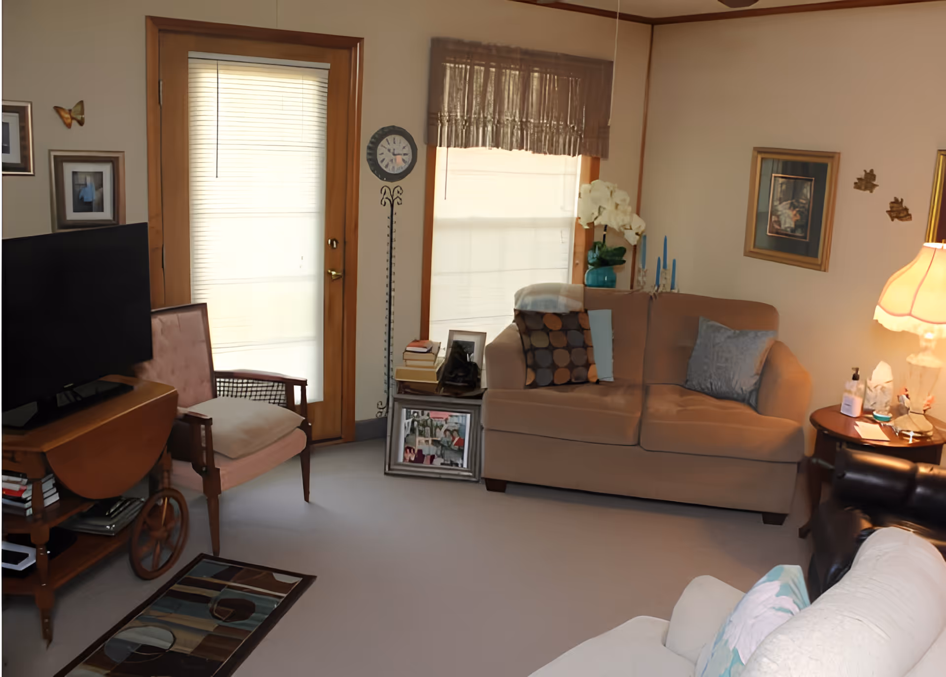 Cozy living room with a beige loveseat, armchairs, TV, side table and a door with window shades.