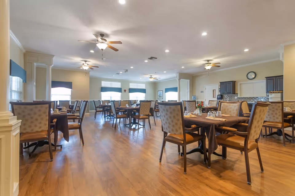 Spacious dining room with multiple tables and upholstered chairs, ceiling fans, and hardwood floors.