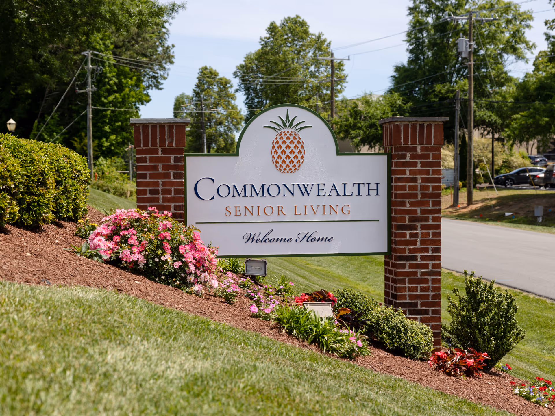 Commonwealth Senior Living entrance sign framed by brick columns with blooming flowers.