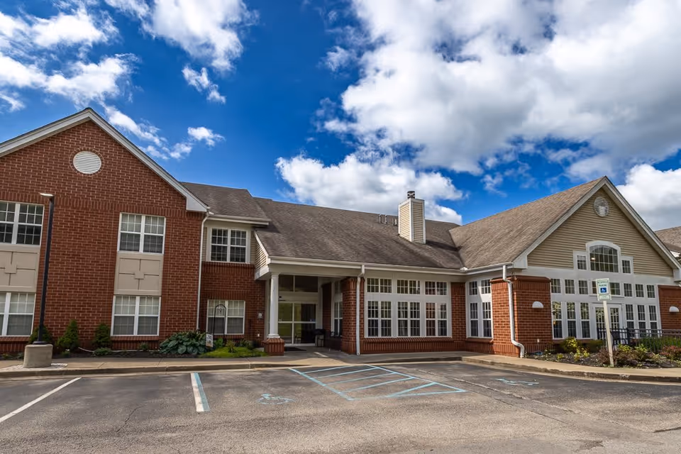 Exterior view of a brick and siding building under a partly cloudy blue sky, showing the entrance with large windows and a parking area with handicap parking spaces in front.