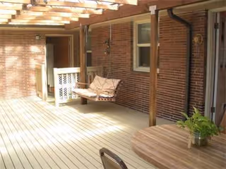 Brick exterior porch with wooden pergola, a swing chair, and round table.