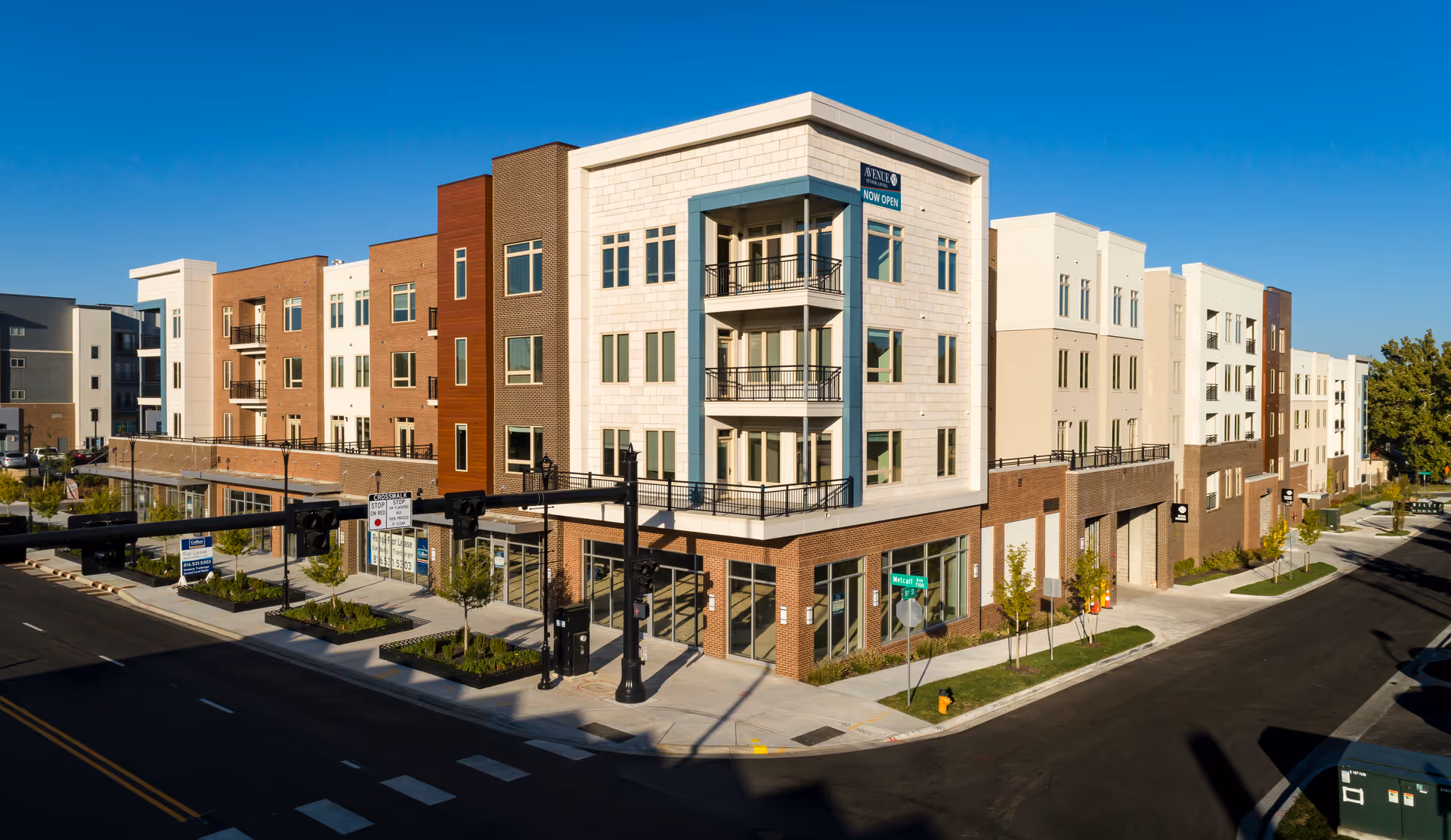 Exterior view of a modern multi-story assisted and independent living facility named Avenue 81 Assisted & Independent Living, located at a street corner with clear blue sky above. The building features a mix of brick and light-colored paneling with multiple windows and balconies.