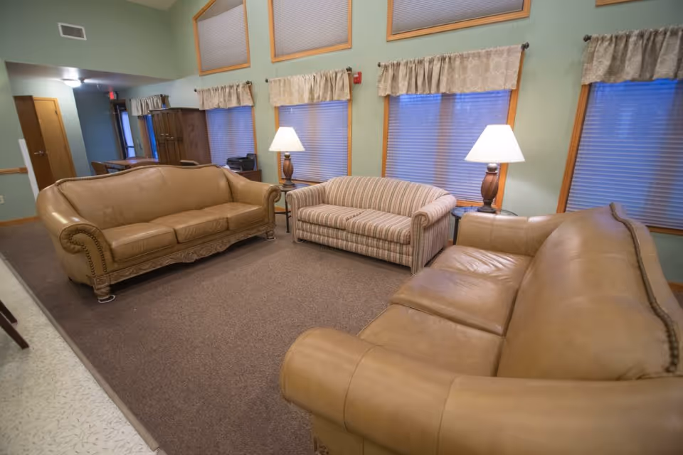 A cozy living room with three sofas, two table lamps, and multiple windows with blinds and valances.