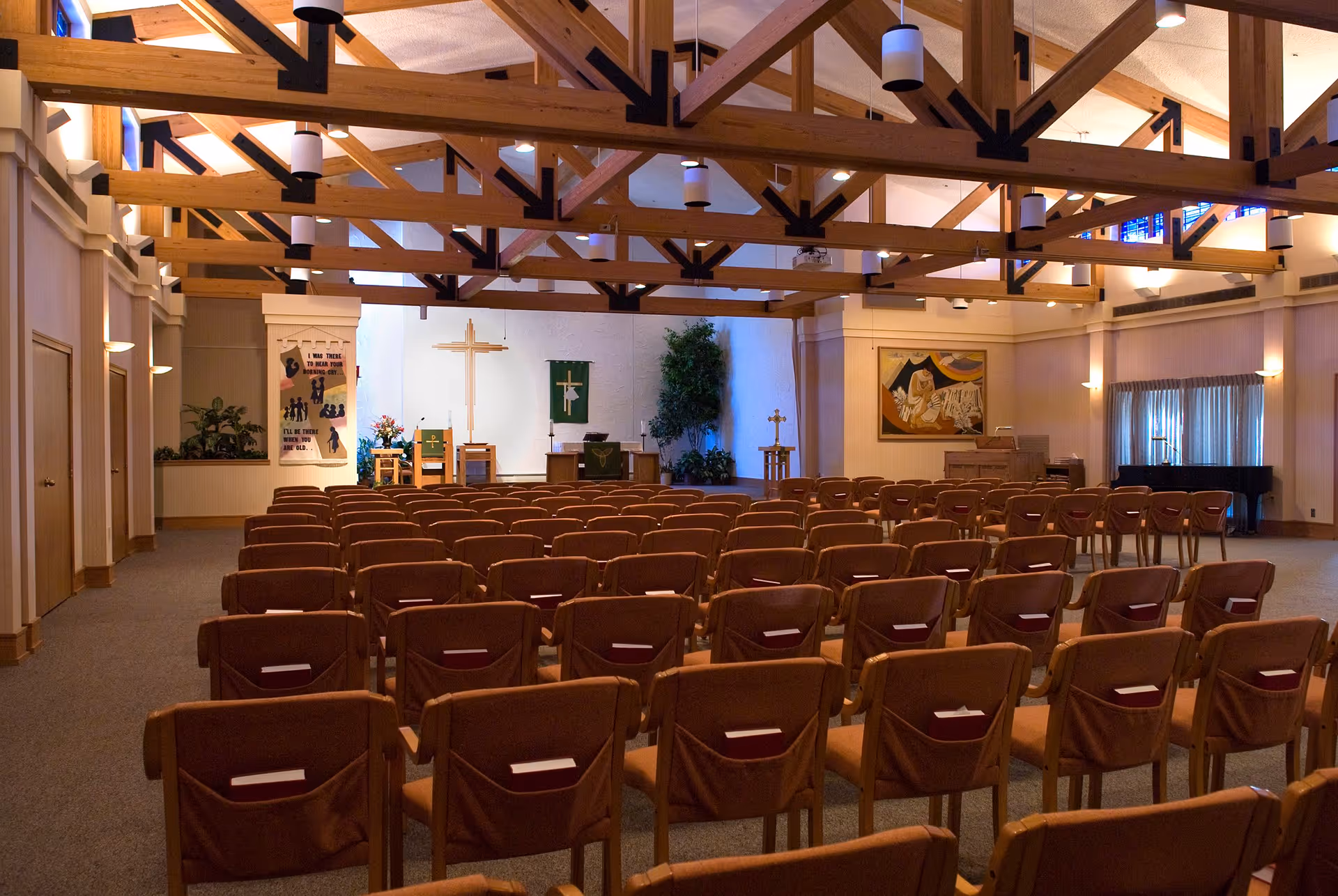 Rows of chairs facing an altar and a cross in a chapel-style assembly room with exposed wooden ceiling beams.