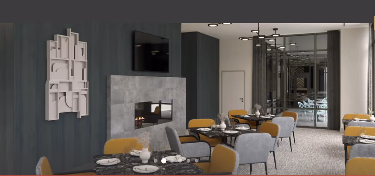 A modern dining room with multiple tables set for meals, featuring gray and mustard yellow chairs. A fireplace with a mounted TV above it is on one wall, and there is abstract wall art next to the fireplace. Large windows with curtains are visible in the background.