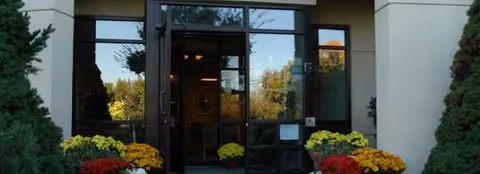 Front entrance of Havencare at Hancock Hall with glass doors and colorful flowers.