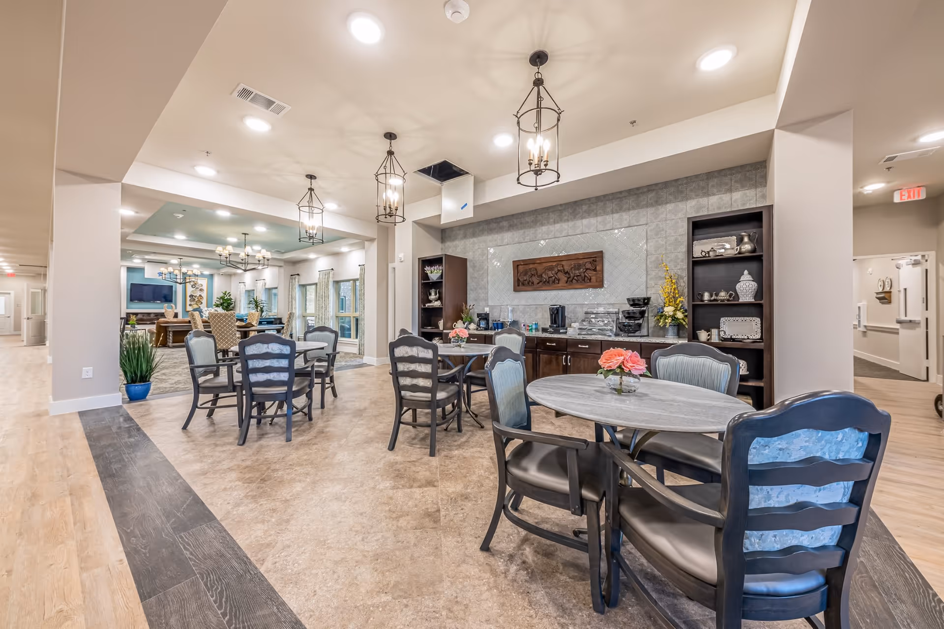 Senior living dining area with round tables, chairs, and a beverage station in a bright lounge.
