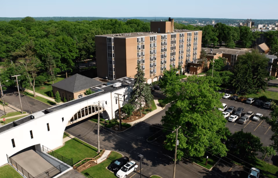 Aerial view of Park Vista of Youngstown facility showing a multi-story building connected by a white elevated walkway over a road, surrounded by trees and a parking lot with several cars.