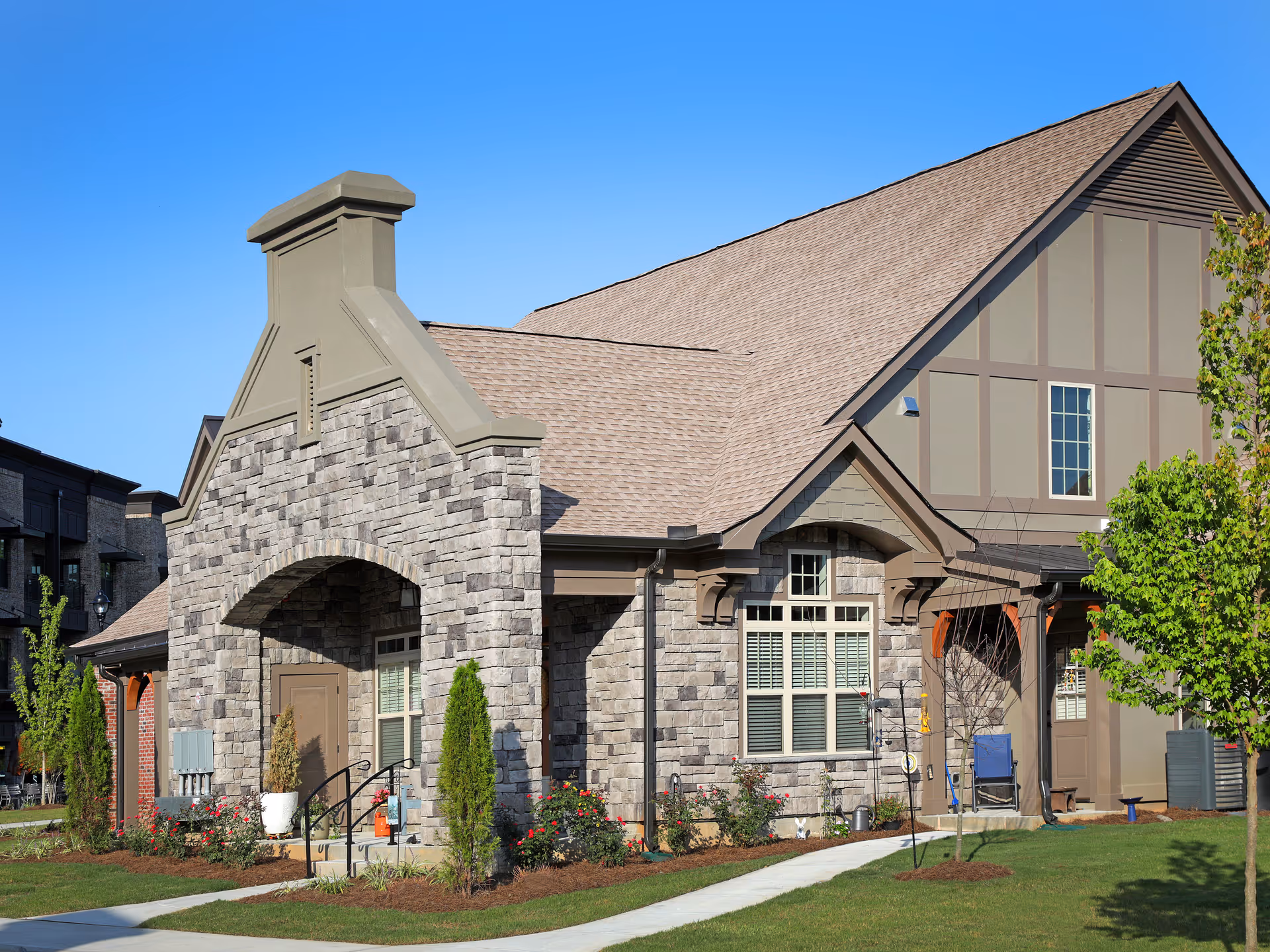 Front exterior of a stone-faced residential building with an arched entry, gabled roof, and landscaped lawn.