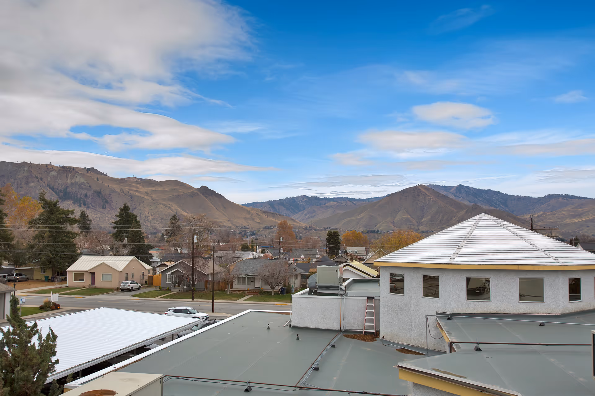 View over building rooftops and a small neighborhood toward rolling hills under a blue sky.