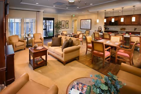 Bright, well-lit communal living and dining area with sofas, armchairs, dining tables and a kitchenette in the background.