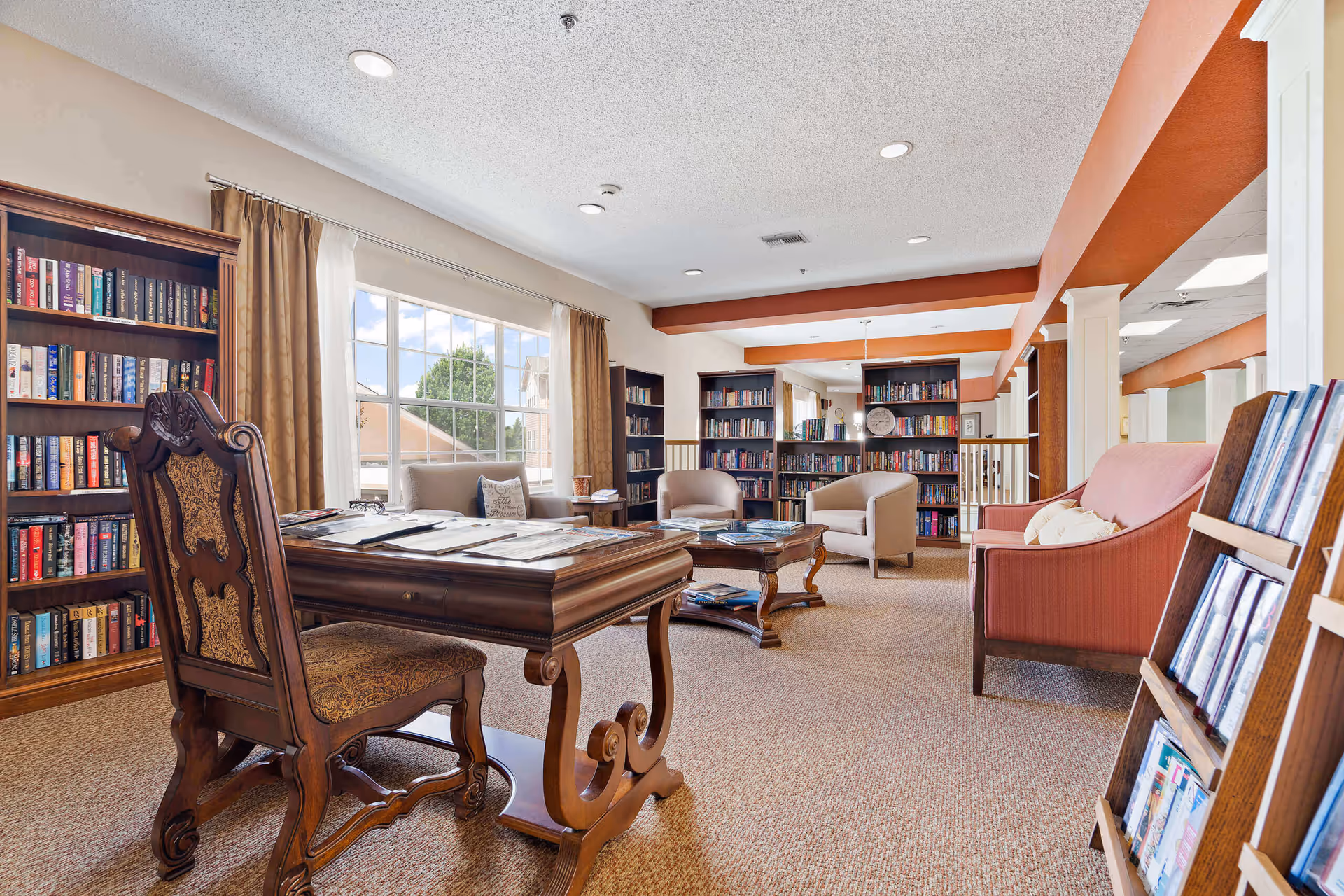 Bright, cozy library-style common room with bookshelves, a wooden desk, and seating area.