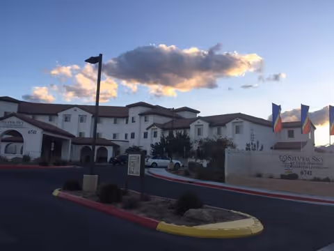 Exterior view of Silver Sky at Deer Springs Assisted Living with entrance, flags, and curved driveway.
