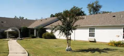 White single-story senior living building with a curved walkway and small tree in front yard.