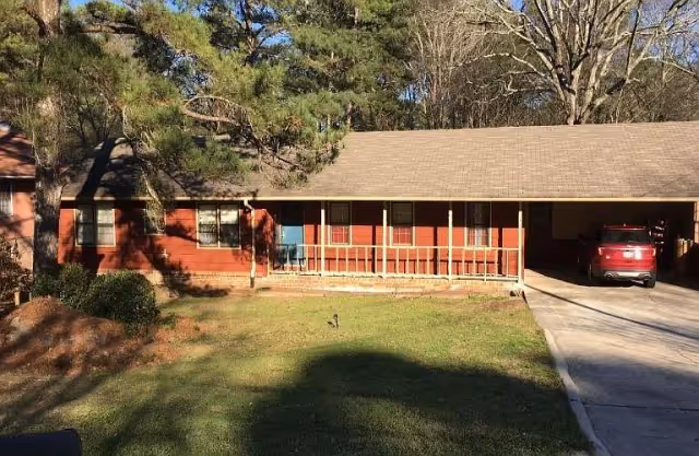 Front exterior of a single-story brick house with a covered porch, carport, and a red SUV in the driveway.