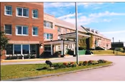 Front entrance and facade of a multi-story brick senior care facility with a covered drop-off and landscaped circular driveway.
