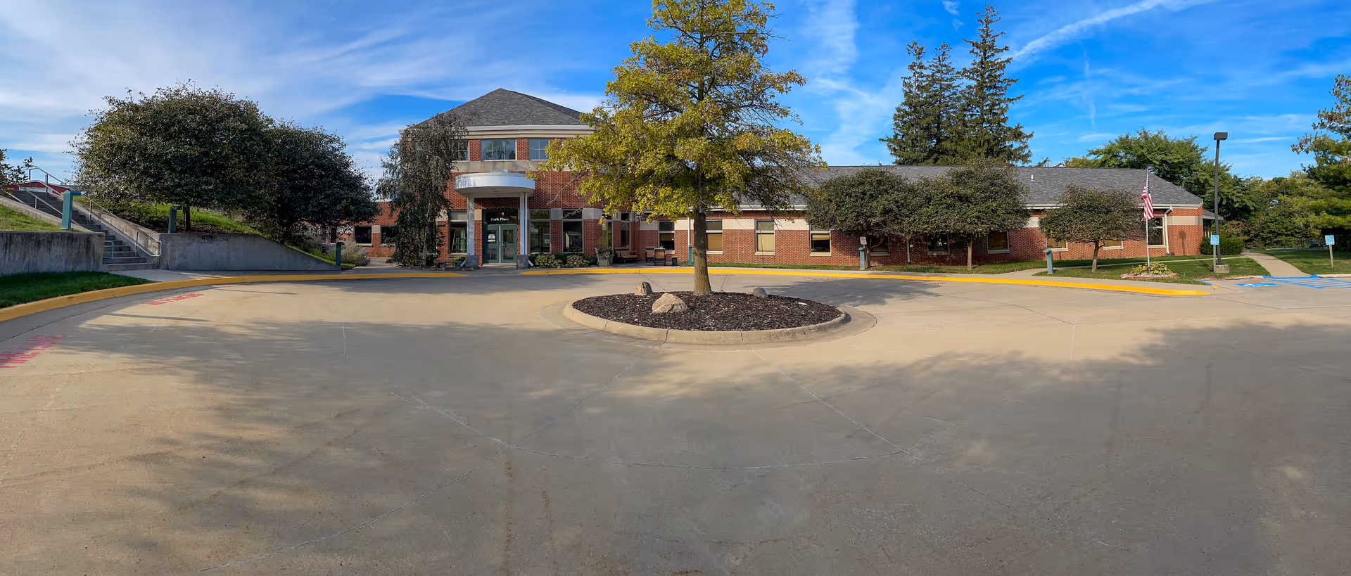 Front exterior of a red-brick long-term care building with a circular driveway and a tree in the center.