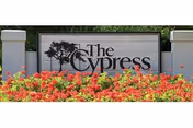 A large sign for The Cypress of Hilton Head featuring the text 'The Cypress' with a tree graphic on the left side, surrounded by a bed of red and orange flowers in front of the sign.