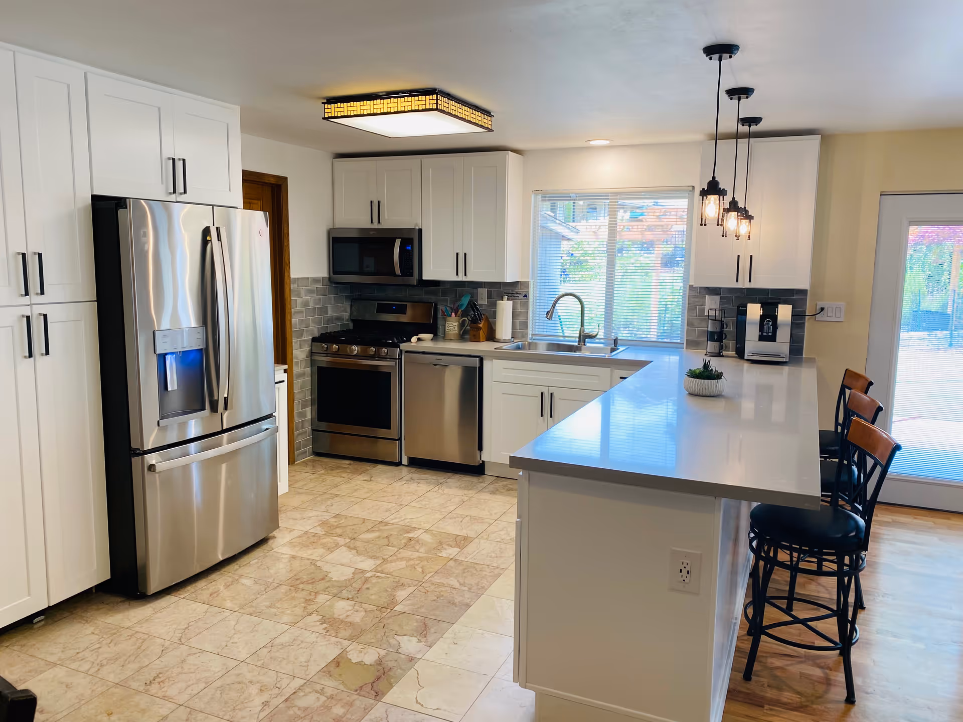 Bright modern kitchen with white cabinets, stainless steel appliances, a long island with bar stools, and a window over the sink.