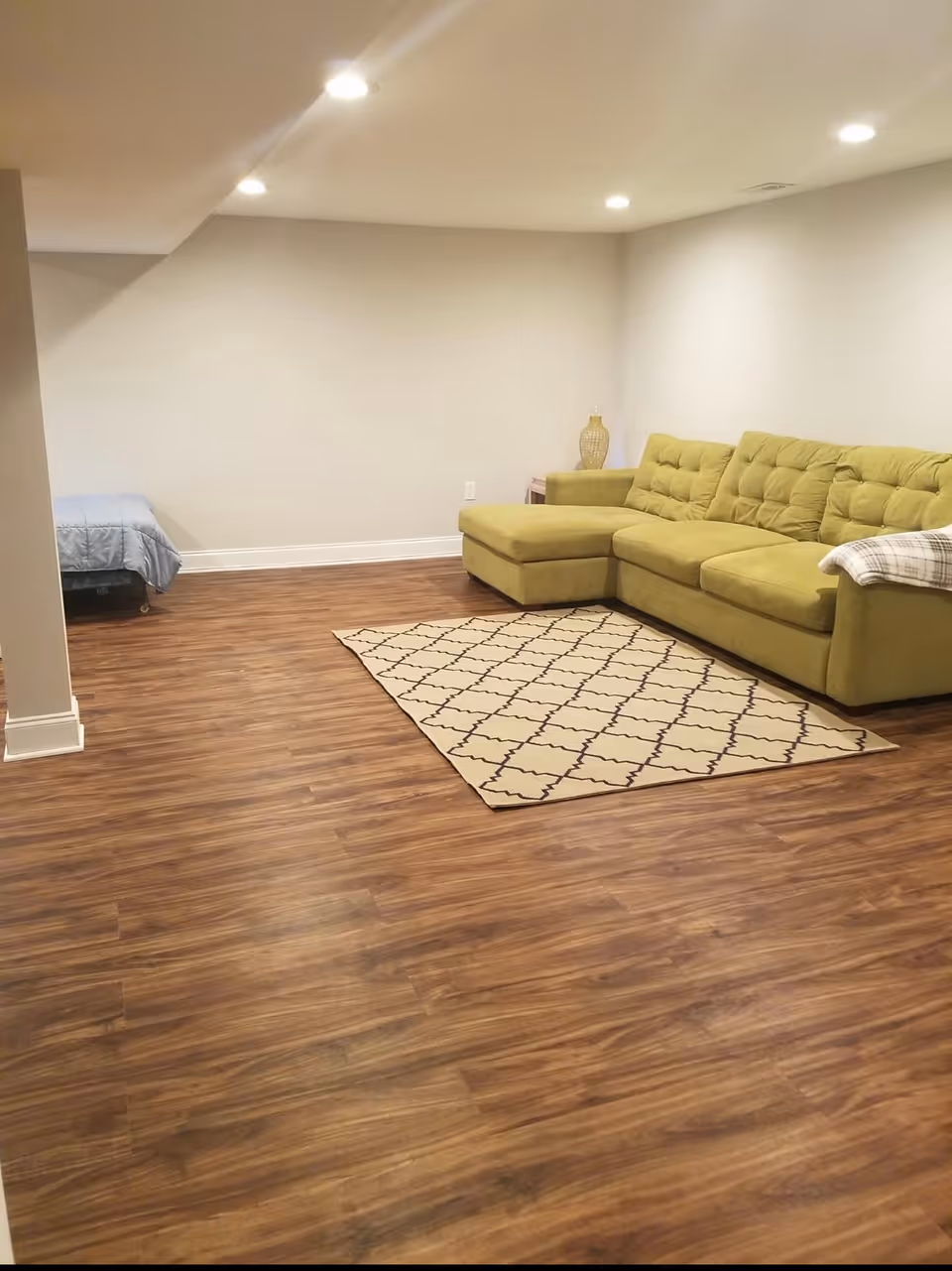 Open living room with a green sectional sofa, patterned rug, and wood-look flooring.